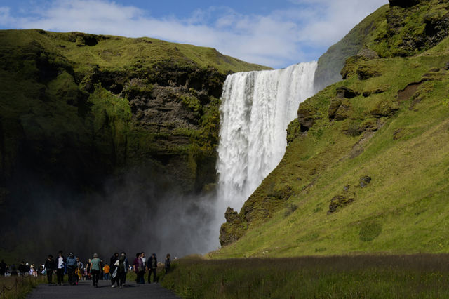 Majestic waterfall cascades down green, mossy cliffs under blue sky.