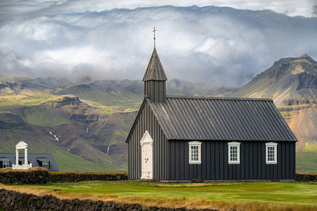 Búðakirkja, the famous Black Church of Búðir, on the Snæfellsnes Peninsula stands in Iceland’s wild landscape, framed by dramatic mountains and moody clouds.