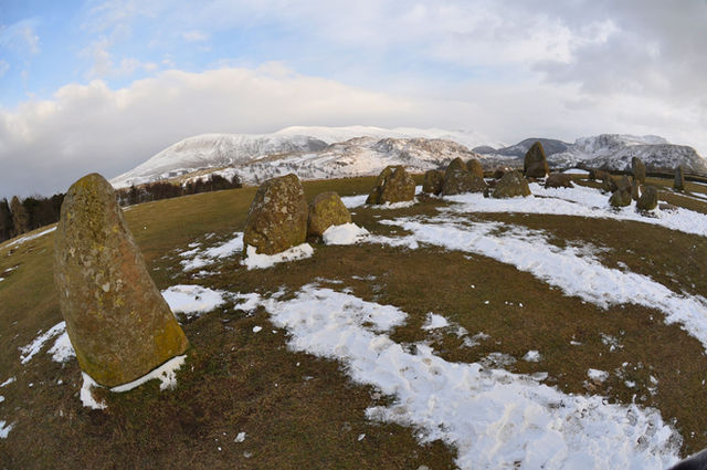 Captivating winter view of Castlerigg Stone Circle with snow-covered hills in the Lake District, England.