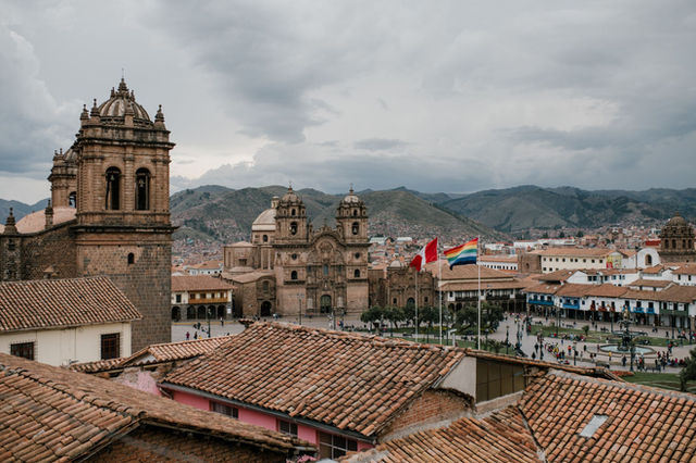 High angle of shabby tile roofs of old buildings and Plaza De Armas with national flags and church in Cusco Peru