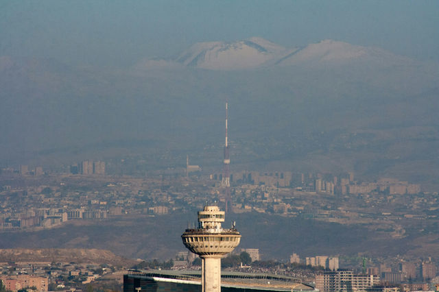 City skyline with a tall tower and distant mountains.