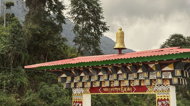 A beautifully decorated gateway with golden and red details stands at the edge of lush greenery in Phuentsholing, Bhutan, blending tradition and spirituality with the mountain landscape.