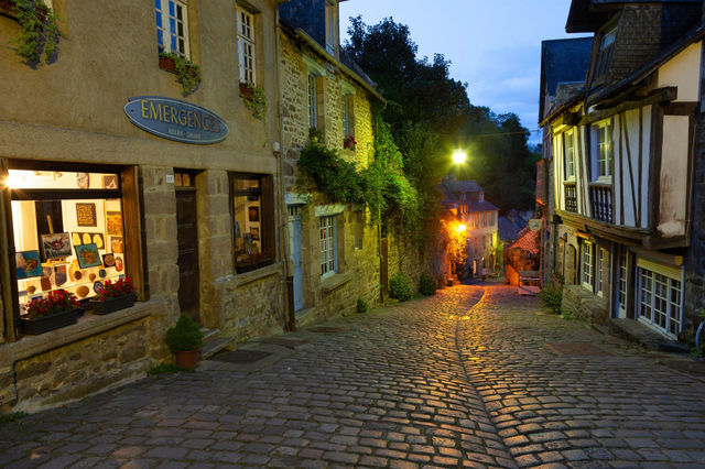Charming cobblestone street in Dinan, Brittany, France, illuminated during dusk. A perfect blend of old-world architecture and evening glow.