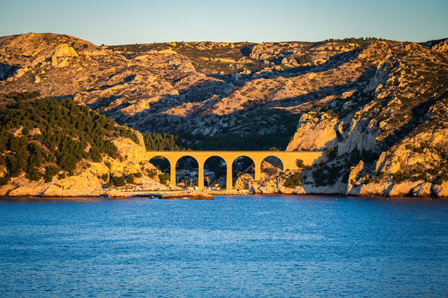 Stunning view of the arch bridge in Marseille, Provence with golden sunset hues over the Mediterranean Sea.