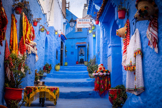 Colorful blue alleyway in the medina of Chefchaouen, Morocco with traditional textiles.