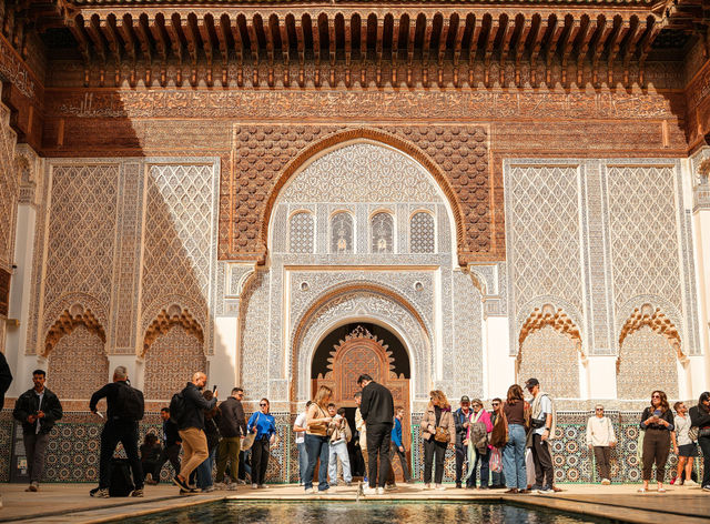 Group of tourists exploring Ben Youssef Madrasa's intricate architecture in sunny Marrakech.