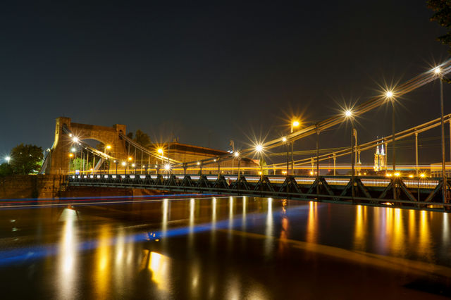 An illuminated bridge reflects in the water at night.