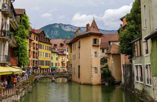 Picturesque canal and historic buildings in Annecy, framed by lush greenery and mountain views.