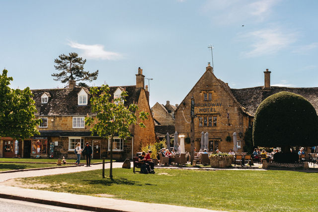 A picturesque day in a Cotswolds village featuring historic architecture and vibrant outdoor activity.