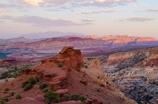 Colorful red rocks, striped cliffs, mountains in the distance, and a pale blue moving to purple sky.