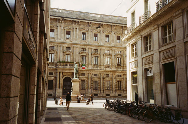 Explore a charming Milan square with classic architecture and a statue in vibrant sunlight.