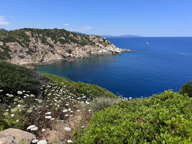 Breathtaking view of Sardinia's coast with a sailboat on the horizon under blue skies.