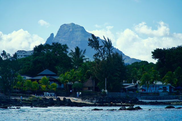 Mountain peak towering over a coastal village and lush trees.