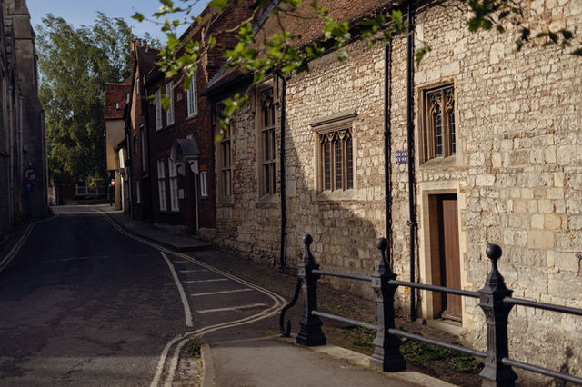 a narrow street lined with stone buildings and a metal fence