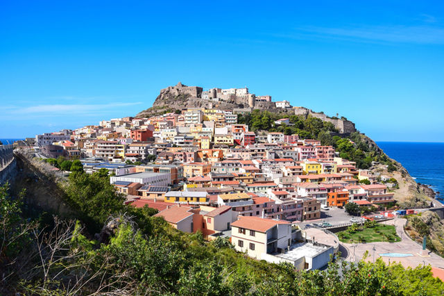 A stunning view of Castelsardo, Sardinia, showcasing vibrant buildings and a historic castle by the sea.