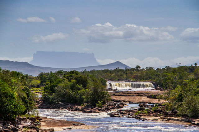 Breathtaking view of a waterfall with lush greenery and a distant Tepui in Canaima National Park, Venezuela.