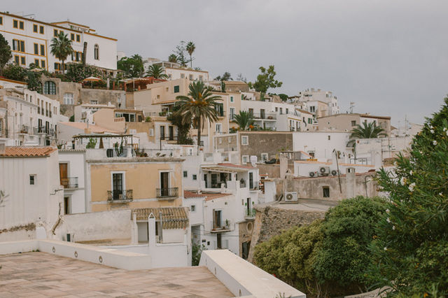 Charming hillside view of traditional white buildings in Ibiza, Spain, with lush greenery and cloudy skies.