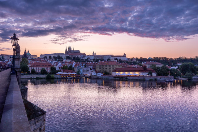 Stunning view of Prague Castle from Charles Bridge during sunset, reflecting in the Vltava River.