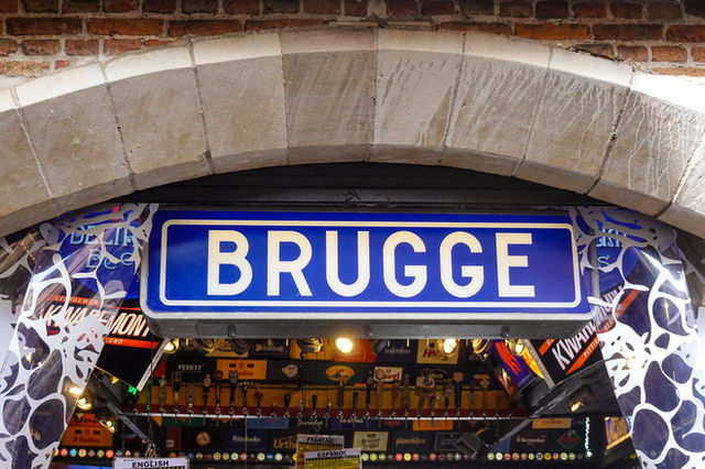 Sign marking entrance to a shop in Bruges, Belgium, featuring classic brick archway architecture.