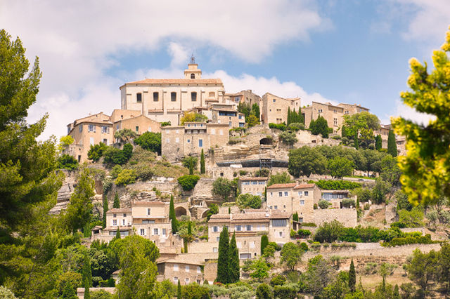 Charming hillside village of Gordes in Provence, showcasing historic architecture and lush greenery.