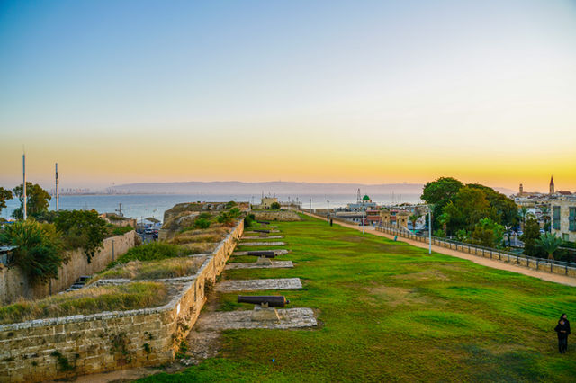 Ancient stone walls with green grass and distant city skyline.