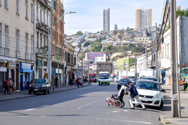 Street scene in Valparaíso with colorful buildings, vehicles, and pedestrians on a sunny day.