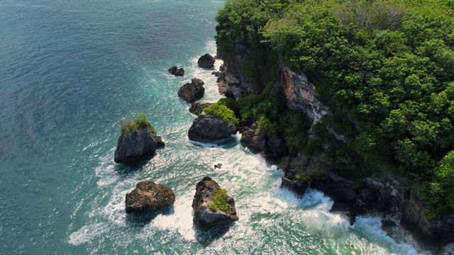 Stunning aerial view of a rocky coastline with lush greenery in Bali, Indonesia.