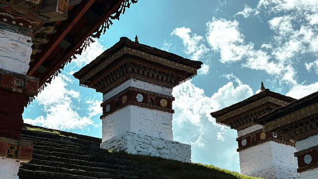 Sunlight illuminates the white stupas of Dochula Pass against a bright blue sky, highlighting their intricate details and serene Himalayan setting.