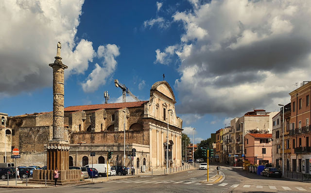 Street view of historic architecture and column in Sassari, Sardinia under a vibrant sky.