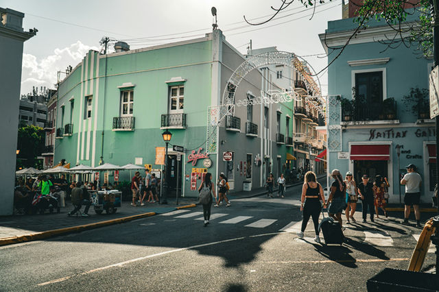 People walk on a sunny street with colorful buildings