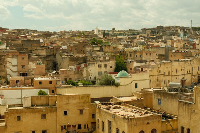 Aerial view of Fes city showcasing historic architecture and rustic rooftops under a cloudy sky.
