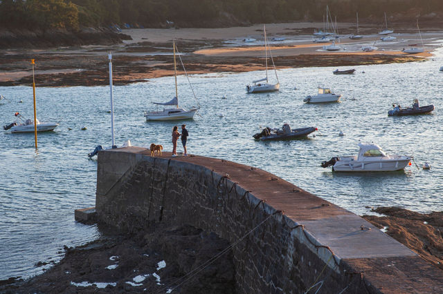 Scenic view of a couple with a dog on a stone pier in Brittany with moored boats.