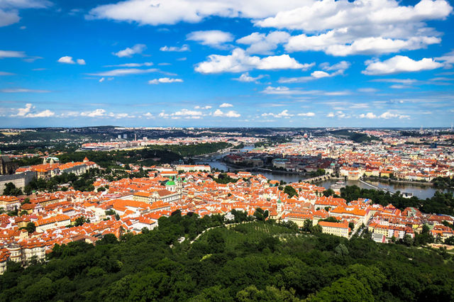 A captivating aerial view of Prague's historical cityscape with landmarks, rooftops, and greenery under a blue sky.