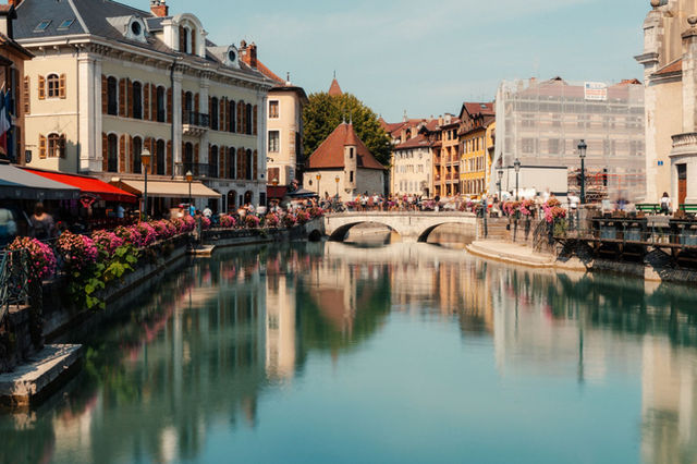 Picturesque canal scene in Annecy, France with historic buildings and a scenic bridge reflecting in the water.