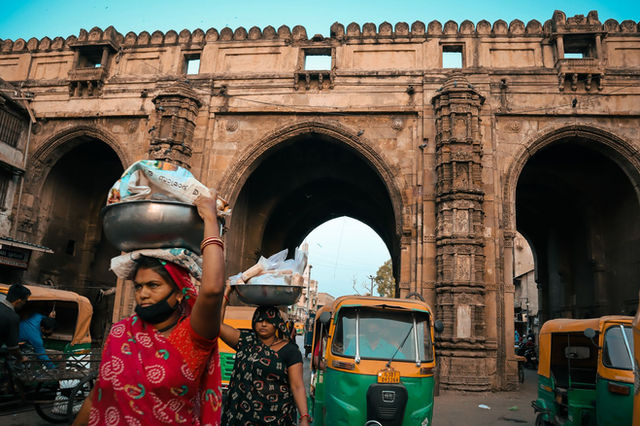 Street vendors and auto-rickshaws bustle by a historic gate in Ahmedabad, India.