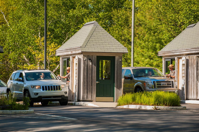 Two small, booth-like buildings are positioned across a roadway. Park rangers are seated at open win