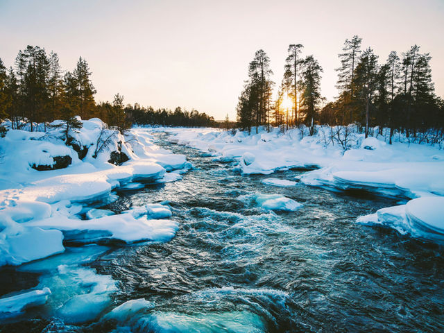 The Juutuan river at Inari in Finland isn't frozen even in winter. The sun ist going down and it's rather early about 3 p.m.