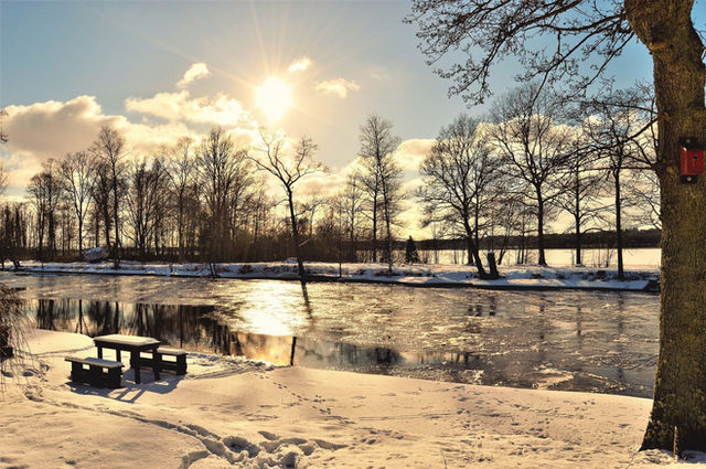 Serene winter sunset scene with snow-covered banks and a frozen river in Norrtälje, Sweden.