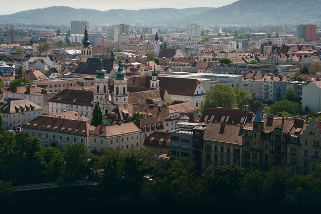 Aerial view of Graz, Austria showing historic architecture, churches, and lush greenery.