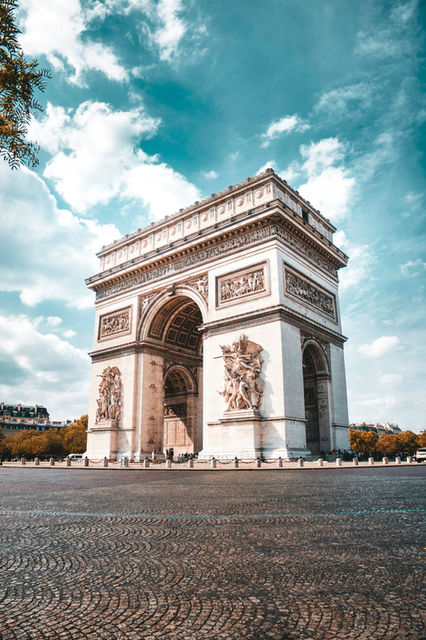 The Arc de Triomphe in Paris under a bright blue sky with clouds