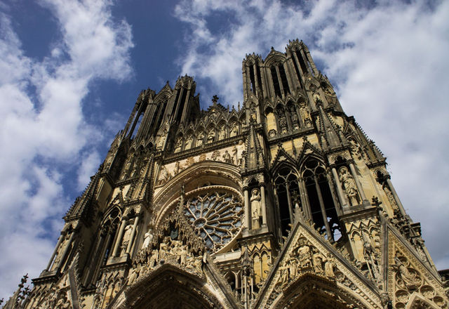 Low angle shot of Reims Cathedral showcasing Gothic architecture against blue sky.