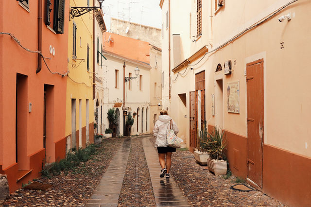 Woman walking through a colorful cobblestone alley in Alghero, Sardinia, Italy.