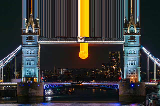 Orange moon perfectly framed by london's tower bridge at night.