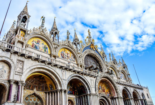 Low angle view of the ornate facade of St. Mark's Basilica under a blue sky in Venice, Italy.