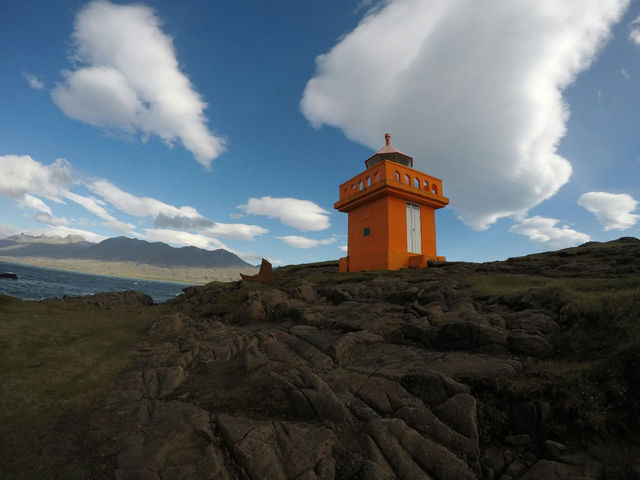 Orange lighthouse on a rocky hill under clouds
