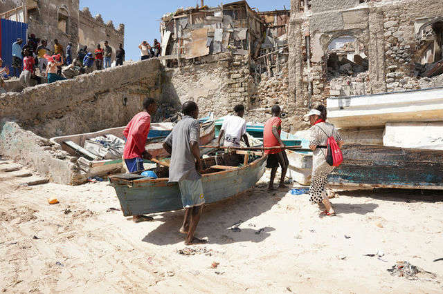 Men work on a boat on a sandy shore.