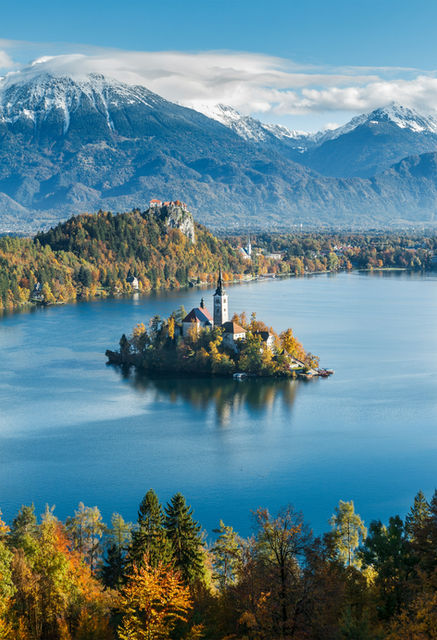 a small island with a building on it surrounded by trees and mountains