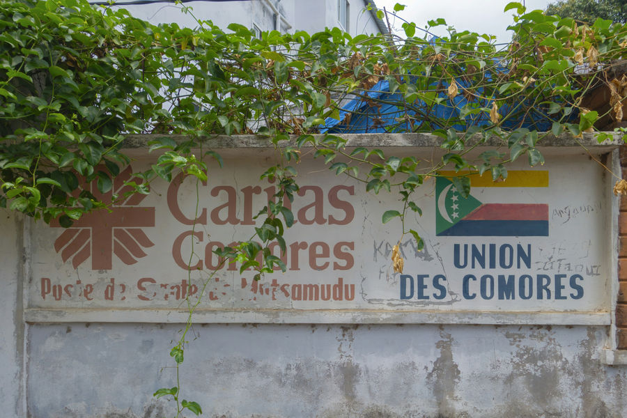 Une vieille pancarte Caritas Comores, usée par le temps, au bord du chemin.
