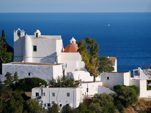A picturesque view of a white church on Ibiza's coast, set against the tranquil blue Mediterranean Sea.