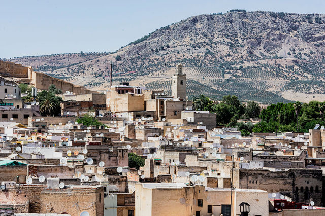 A detailed aerial view of the historic Fes Medina in Morocco with the Atlas Mountains in the background.